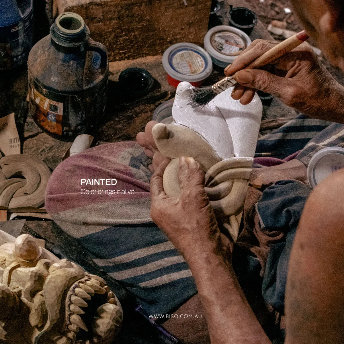 Artisan brushing a white base coat onto a hand-carved Sri Lankan mask – traditional mask painting process