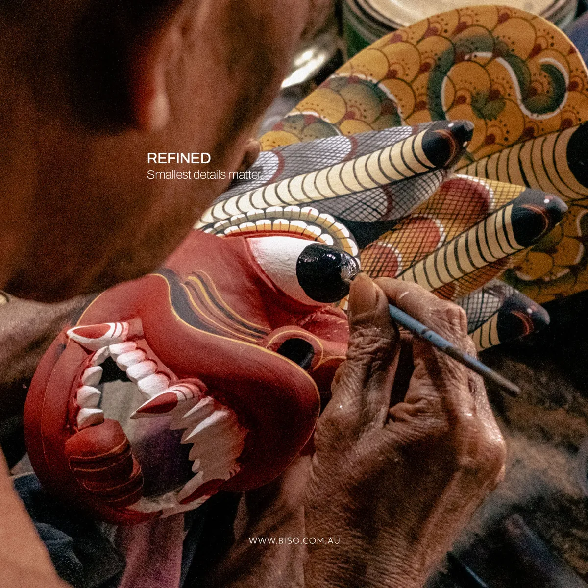 Close-up of an artisan hand painting the eye of a red Naga Raksha mask with a fine brush – genuine handcrafted detail