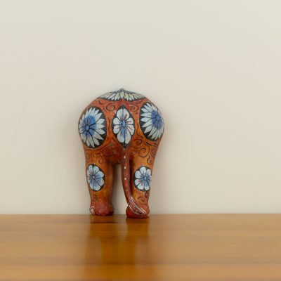 Rear view of a hand-painted Sri Lankan wooden elephant showing blue and white floral motifs on a terracotta background.