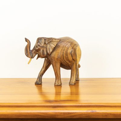 Close up of hand-carved Balinese elephant showing dark natural wood grain lines and upward trunk.