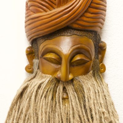 Front view of the large handcrafted wooden mask showing its expressive carved face, warm natural wood tones and distinctive long natural-fibre hair.